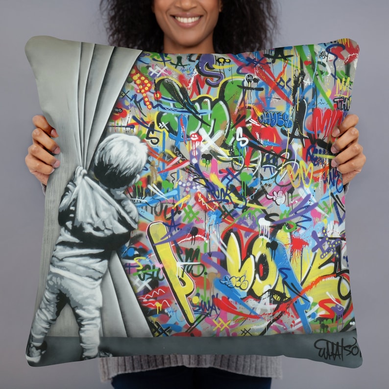 May include: A colorful throw pillow featuring a child peeking around a corner revealing a wall covered in graffiti. The graffiti is in various colors, including red, yellow, blue, green, and purple. The text "What So" is visible in the bottom right corner of the pillow.
