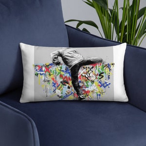 May include: A white throw pillow with a colorful graffiti design featuring a person kicking a wall. The person is wearing a white jacket and jeans.