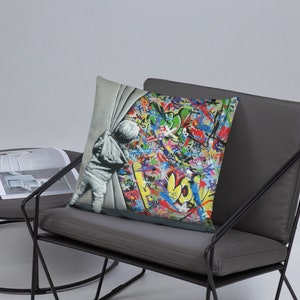 May include: A throw pillow featuring a colorful graffiti background with a child peeking out from behind a white curtain. The child is wearing a grey hooded sweatshirt and pants. The graffiti includes the word "LOVE" in large yellow letters.