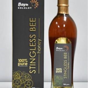 May include: A glass bottle of 100% pure stingless bee honey, labeled "Bayu Kelulut Stingless Bee Honey" with a gold and black design. The bottle is 700 grams and is next to a box with the same design.