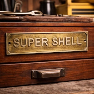 May include: A dark wooden box with a brass plate bearing the words "SUPER SHELL". The box features a drawer with a metal handle. The wood is a deep brown. Tools are visible on the top of the box.