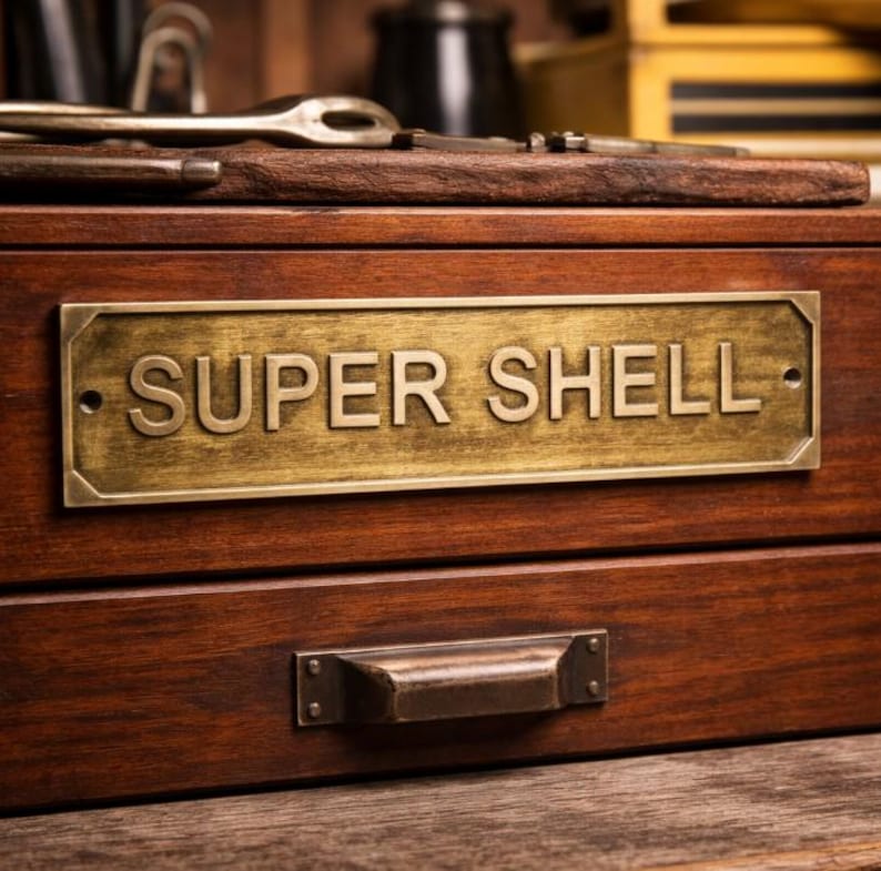 May include: A wooden box with a brass plate that reads "SUPER SHELL". The box has a drawer with a metal handle. The wood has a rich, dark brown color. Tools are visible on top of the box.