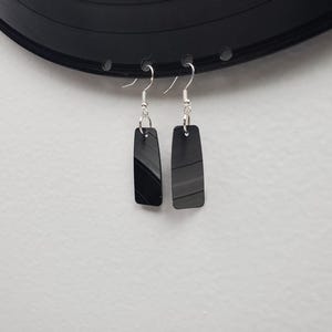May include: A pair of black earrings made from recycled vinyl records. The earrings are rectangular in shape and have a silver hook.