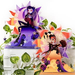 Op de afbeelding: Twee acryl karakter standees met kleurrijke illustraties van animatiefiguren. Eén personage zit op een wolk, de ander houdt een boeket vast. Elke standee heeft een zon- en maanontwerp op de achtergrond.