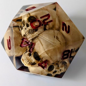 May include: A clear, multi-sided dice with a skull design and red numbers. The numbers on the dice are 2, 4, 5, 6, 7, and 8.