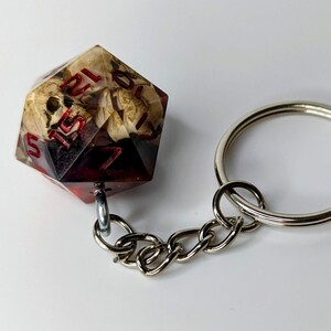 May include: A red and white dice keychain with a skull and crossbones design. The dice is attached to a silver chain and a silver key ring.