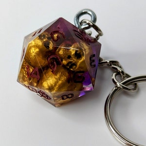 May include: A purple and gold dice keychain with a silver key ring. The dice has numbers 1 through 6 on each side.