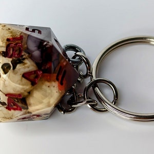 May include: A white and red resin dice keychain with a silver key ring. The dice has a skull design inside.