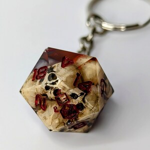 May include: A clear resin dice with a skull design and red numbers. The dice is attached to a silver keychain.