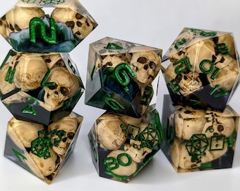 Puede incluir: Seis dados verdes y blancos con diseños de calaveras y huesos. Los dados están hechos de resina transparente y tienen un patrón de remolino verde y blanco. Los dados están numerados del 1 al 6.