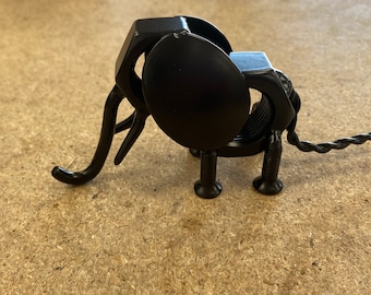 May include: A black metal elephant sculpture made from recycled materials. The elephant has a long trunk, large ears, and four legs. The sculpture is made of nuts, bolts, and other metal pieces.