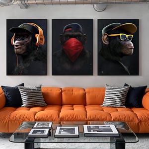 May include: Three framed canvas art prints featuring chimpanzees wearing accessories. One chimp wears headphones and a cap, another a red bandana, and the third, sunglasses and a cap. The art hangs above an orange sofa with decorative pillows.