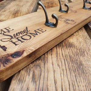 May include: Wooden coat rack with the text "Home Sweet Home" engraved on the front. The rack has five metal hooks and a keyhole design.