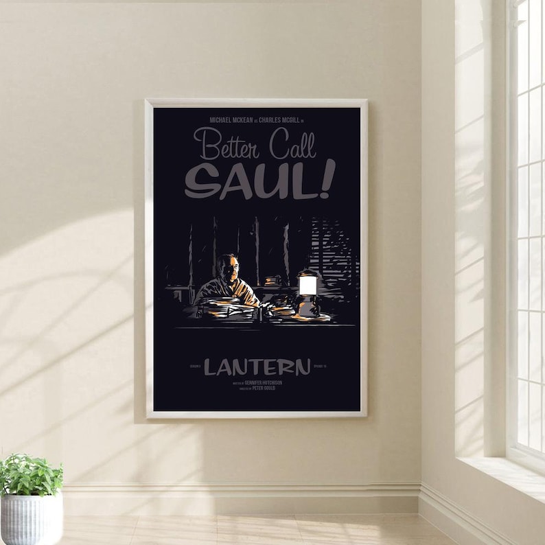 May include: A black and white poster with the title "Better Call Saul!" in a stylized font. The poster features a man sitting at a desk with a lamp on the desk. The poster is framed in a white frame.