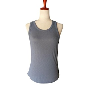 May include: A gray tank top with a scoop neck and ribbed texture. The sleeveless top is displayed on a mannequin with a wooden neck and shoulder form, against a white background. The tank top is a solid color.