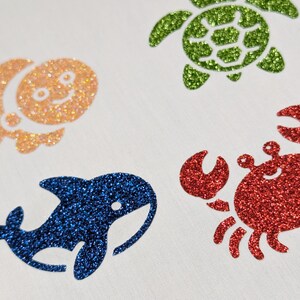 Könnte beinhalten: Vier glitzernde Bügelbilder mit einem blauen Wal, einem roten Krebs, einer grünen Schildkröte und einem orangefarbenen Fisch. Die Bügelbilder befinden sich auf einem weißen Hintergrund.