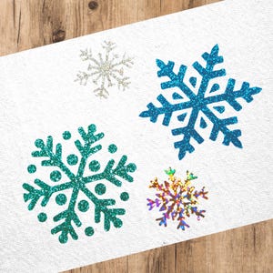 Könnte beinhalten: Vier glitzernde Schneeflocken-Aufkleber in verschiedenen Farben und Designs. Die Schneeflocken sind türkis, blau, silber und regenbogenfarben.