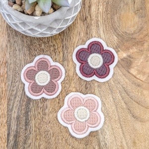 Könnte beinhalten: Drei gestickte Blumenpatches in Rosatönen und Burgunderrot. Die Blumen haben ein schlichtes, Retro-Design mit einer weißen Mitte.