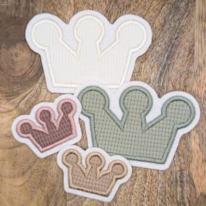 Könnte beinhalten: Drei Filz-Kronen-Patches in verschiedenen Größen und Farben. Die größte Krone ist weiß, die mittlere Krone ist grün und die kleinste Krone ist braun.