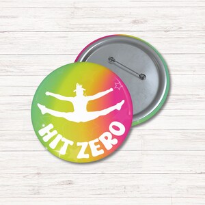 May include: A round button with a colorful gradient background. The background is green, yellow, orange, and pink. A white silhouette of a cheerleader doing a split is in the center of the button. The text "HIT ZERO" is written in white on the button.