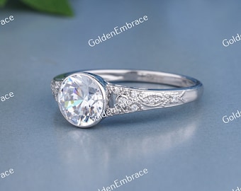 May include: A silver engagement ring with a round, bezel-set diamond and a delicate, engraved band.