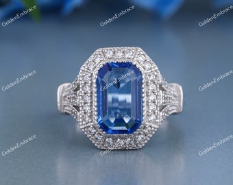 May include: A silver ring with a large, rectangular, blue sapphire gemstone surrounded by smaller diamonds. The ring has a delicate, intricate design.