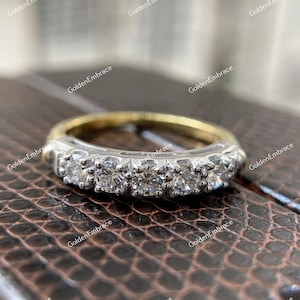 May include: A gold and silver band with a row of small, round diamonds set in a prong setting.