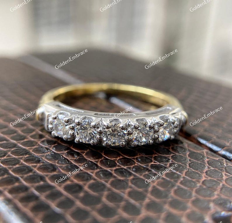 May include: A gold and silver band with a row of small, round diamonds set in a prong setting.