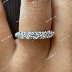 May include: A silver band ring with a row of small, clear, round gemstones. The ring is on a finger.