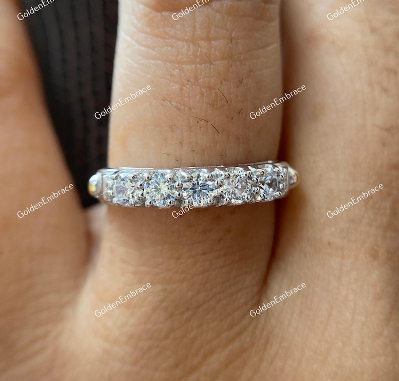 May include: A silver band ring with a row of small, clear, round gemstones. The ring is on a finger.