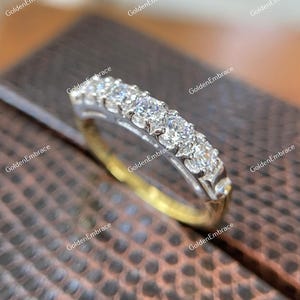 May include: A delicate gold band with a row of sparkling diamonds set in a prong setting. The band is a classic and elegant design that would make a beautiful wedding band or anniversary ring.