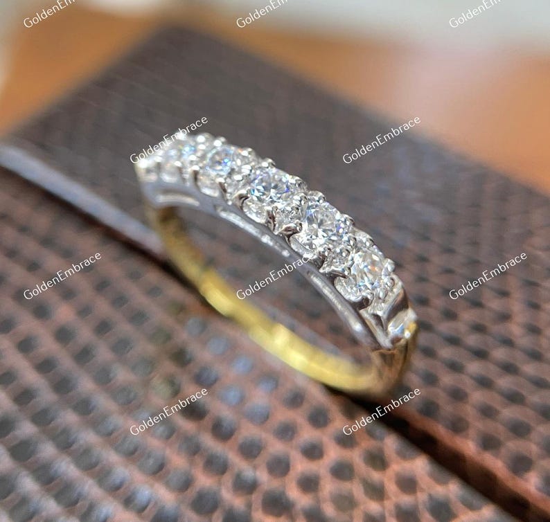 May include: A delicate gold band with a row of sparkling diamonds set in a prong setting. The band is a classic and elegant design that would make a beautiful wedding band or anniversary ring.