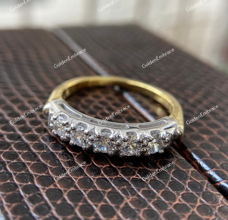 May include: A gold and silver band with a row of sparkling diamonds. The band is set on a brown textured surface.