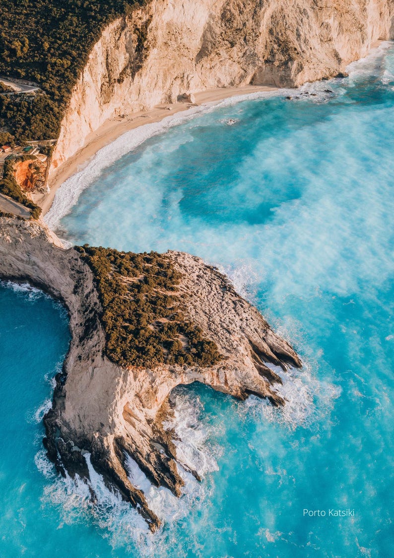 May include: Aerial view of Porto Katsiki beach in Greece. Turquoise water surrounds a rocky cliff covered in green vegetation. Beige cliffs and a sandy beach are visible in the background. The image is taken from a high angle.