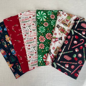 May include: Set of six Christmas-themed fabric napkins featuring various designs, including candy canes, peppermint swirls, nutcrackers, and a Christmas tree. The napkins are in red, green, white, and black.