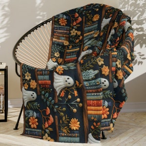 Op de afbeelding: Een donkerblauwe deken met een griezelig, fantasierijk patroon met stapels boeken, geesten en herfstbloemen. Het patroon wordt over de hele deken herhaald.