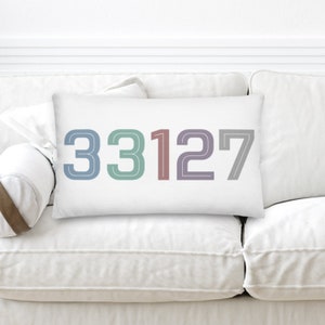 May include: White rectangular pillow with the numbers 33127 in a retro font. The numbers are outlined in black and each number is a different color: blue, green, red, purple, and gray.