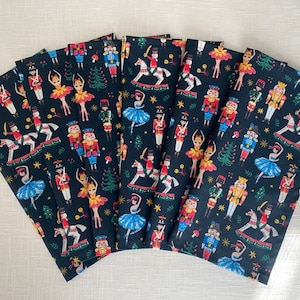 May include: Set of eight black fabric napkins with a repeating pattern of nutcracker soldiers, ballerinas, and Christmas trees. The pattern is in shades of red, green, blue, yellow, and white.