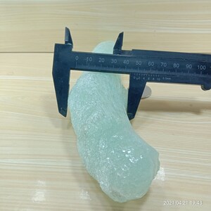 May include: A light green, translucent, irregularly shaped piece of glass being measured with a caliper. The caliper reads 0 to 100 millimeters.