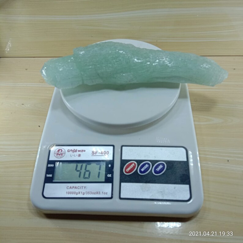 May include: A green, translucent, elongated rock-like object is placed on a digital kitchen scale. The scale reads 461 grams. The scale is white with black buttons labeled "Tare", "Mode", "On/Off", and "Zero". The scale also has a display that shows the weight in grams and ounces. The scale has a capacity of 10000 grams or 353 ounces.
