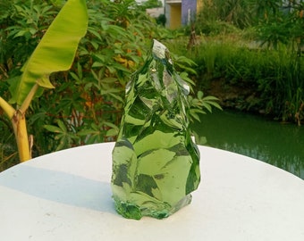 May include: A large, green, glass sculpture with a jagged, irregular shape. The sculpture is sitting on a white surface.