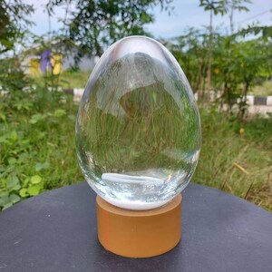 Pode incluir: Um ornamento de vidro transparente em forma de ovo com uma base dourada. O ornamento est&aacute; sobre uma superf&iacute;cie preta.