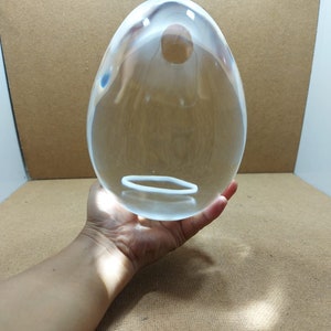 Pode incluir: Um ovo grande de vidro transparente com um anel branco no meio. O ovo est&aacute; sendo segurado na m&atilde;o de uma pessoa.