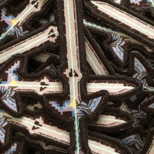 May include: A stack of embroidered patches featuring a pixelated sword design. The sword is white with a light blue and purple glow. The patches are black with a white outline.