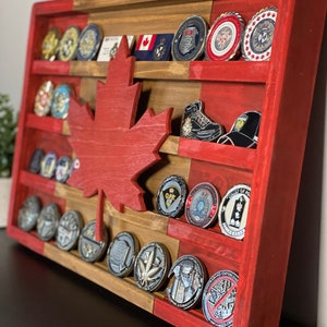 May include: A wooden Canadian flag coin display with a red maple leaf cutout. The display has multiple shelves for holding coins and other memorabilia. The shelves are painted red and brown.