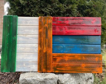 Op de afbeelding: Een houten vlag met groene, witte, rode, blauwe en oranje strepen. De vlag is gemaakt van afzonderlijke houten planken die in de kleuren van de vlag zijn geschilderd.