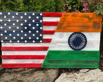 Op de afbeelding: Een houten bord met de Amerikaanse en Indiase vlaggen naast elkaar. De Amerikaanse vlag bevindt zich links en de Indiase vlag rechts. De vlaggen zijn in hun respectievelijke kleuren geschilderd en de Indiase vlag heeft een blauw wiel in het midden.