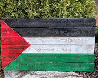 Op de afbeelding: Een houten vlag van Palestina met zwarte, rode, witte en groene strepen. De vlag is gemaakt van afzonderlijke houten planken die in de kleuren van de Palestijnse vlag zijn geschilderd.