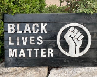 Op de afbeelding: Houten bord met de tekst "Black Lives Matter" in witte letters en een symbool van een opgeheven vuist.