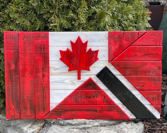 Op de afbeelding: Een houten Canadese vlag met een rood esdoornblad en een zwarte diagonale streep op een witte achtergrond.